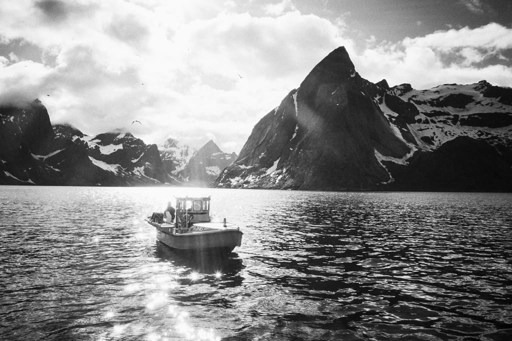 Black and white image. Boat on the sea with mountains in the background.